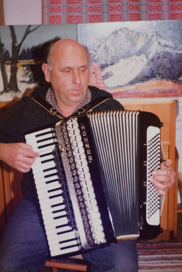 Konrad Sommer spielt Akkordeon, im Hintergrund seine Gemälde, Farbfotografie, um 1980